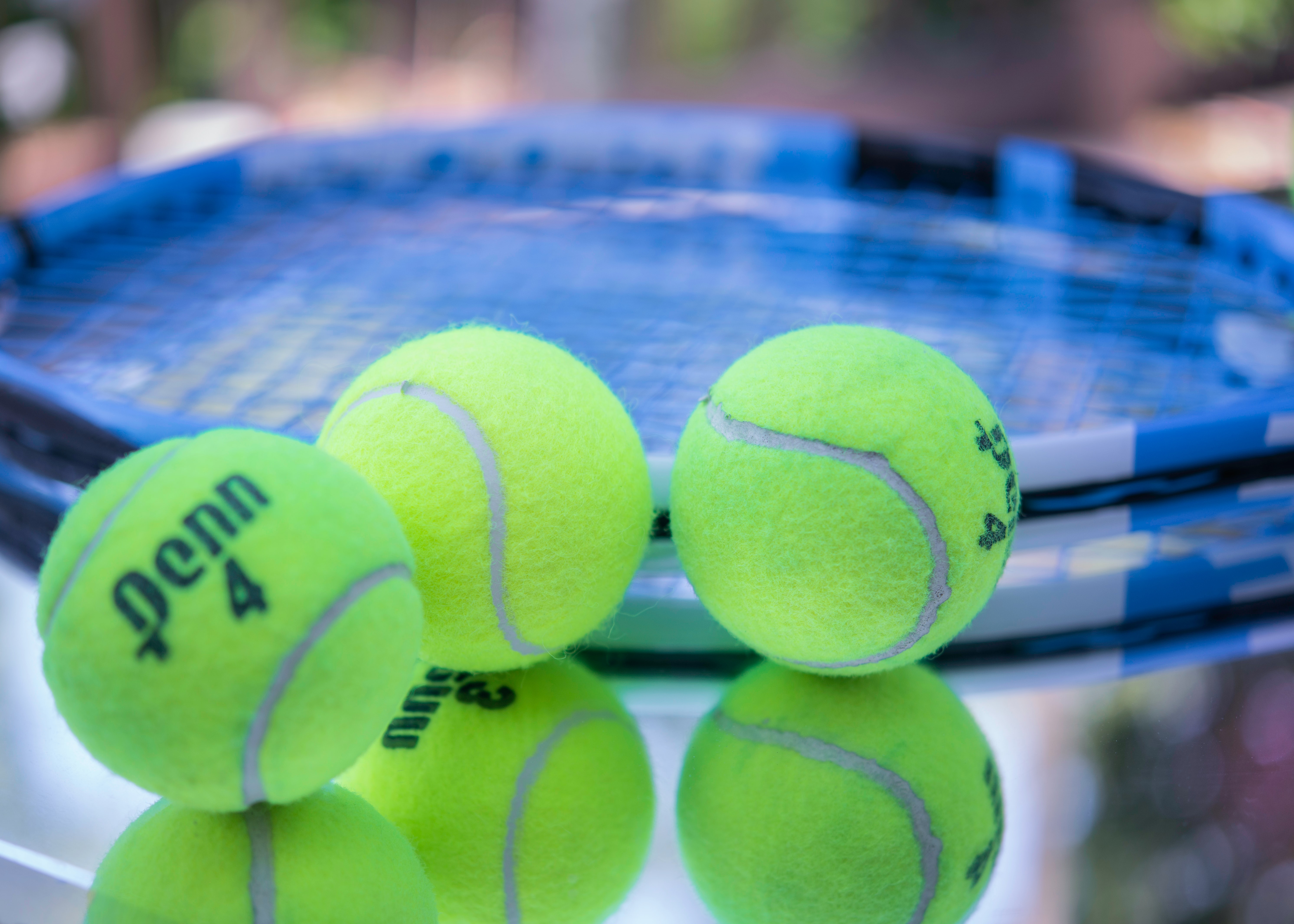 Three tennis balls lying next to a racket